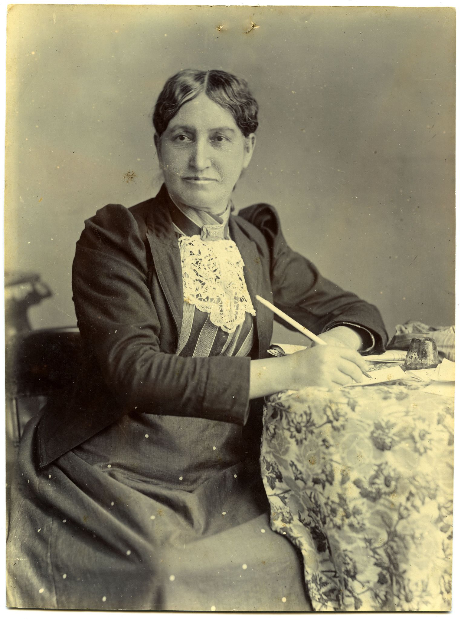 Elizabeth Yates looks off to the side of the camera while signing a document (the women's suffrage petition).